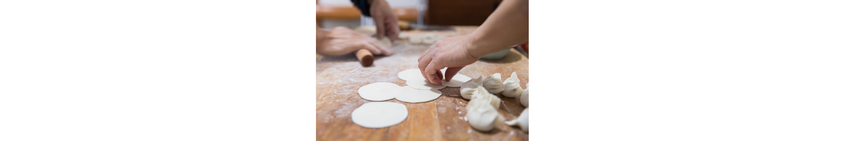 Two people working together at a kitchen table preparing dumplings from scratch.