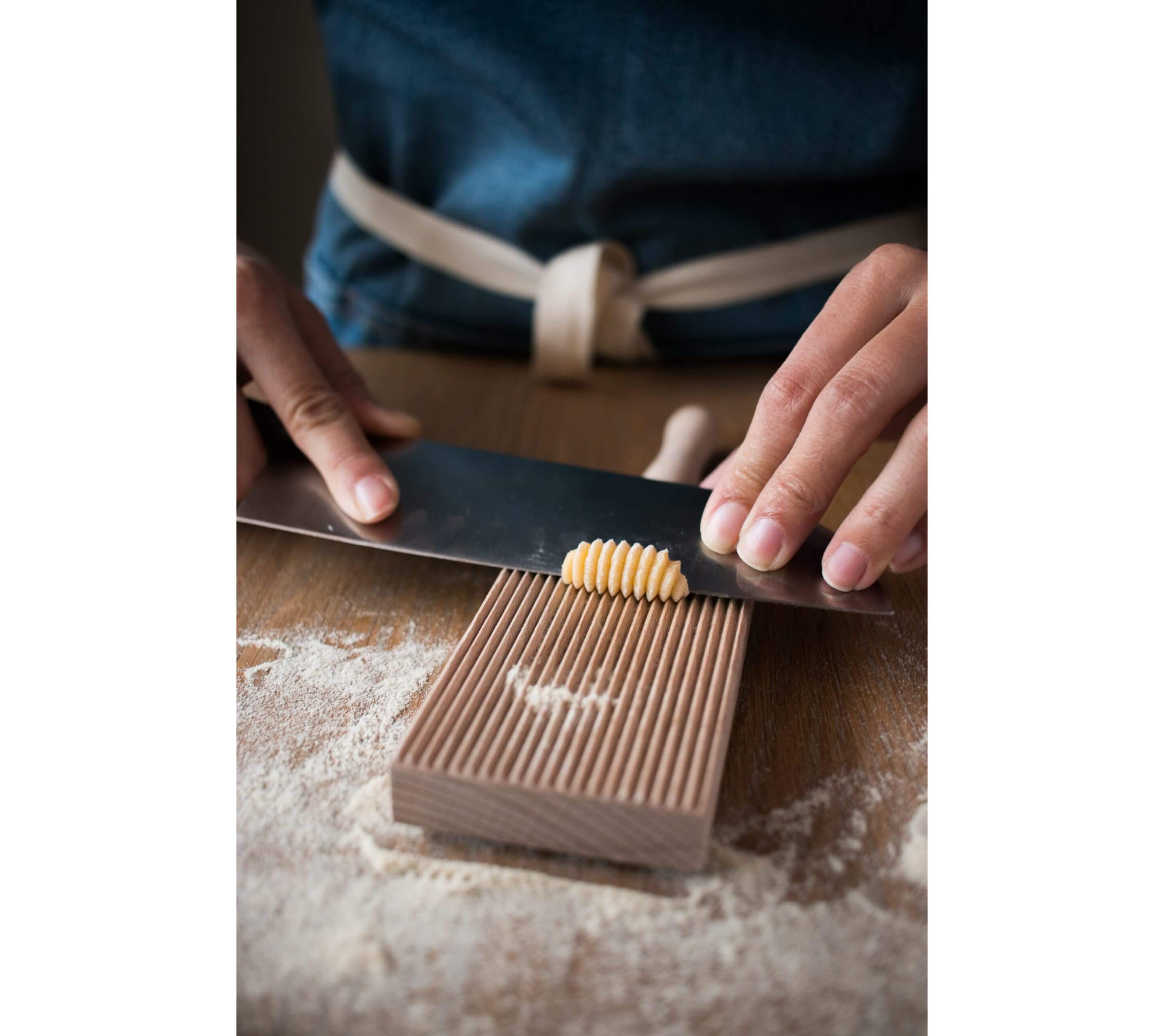 Experienced hands rolling out homemade gnocchi on a gnocchi roller board with a chef's knife.