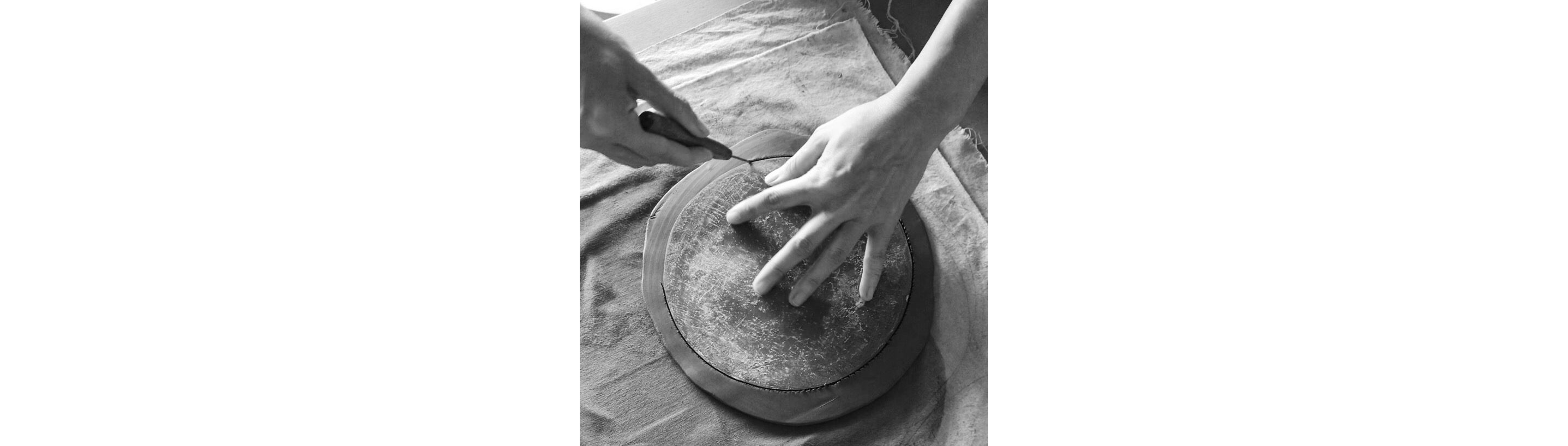 A hand gently trimming clay around a flat disc.