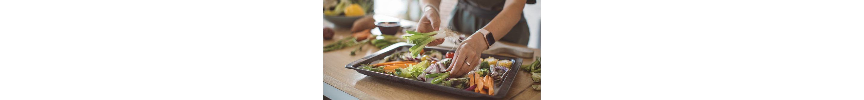 A woman neatly placing green onions on a baking sheet filled with chopped vegetables.