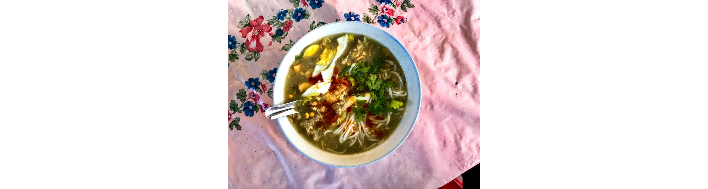 A bowl of mohinga on a floral table cloth.