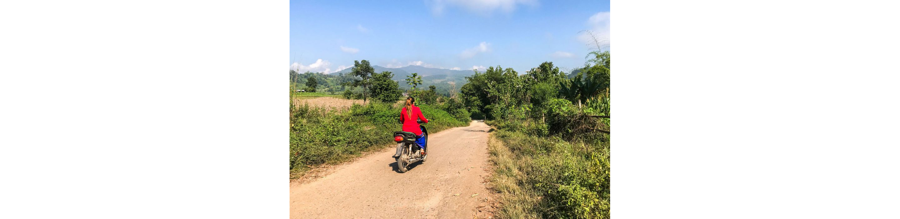 A woman riding a motorized scooter through rural Myanmar.