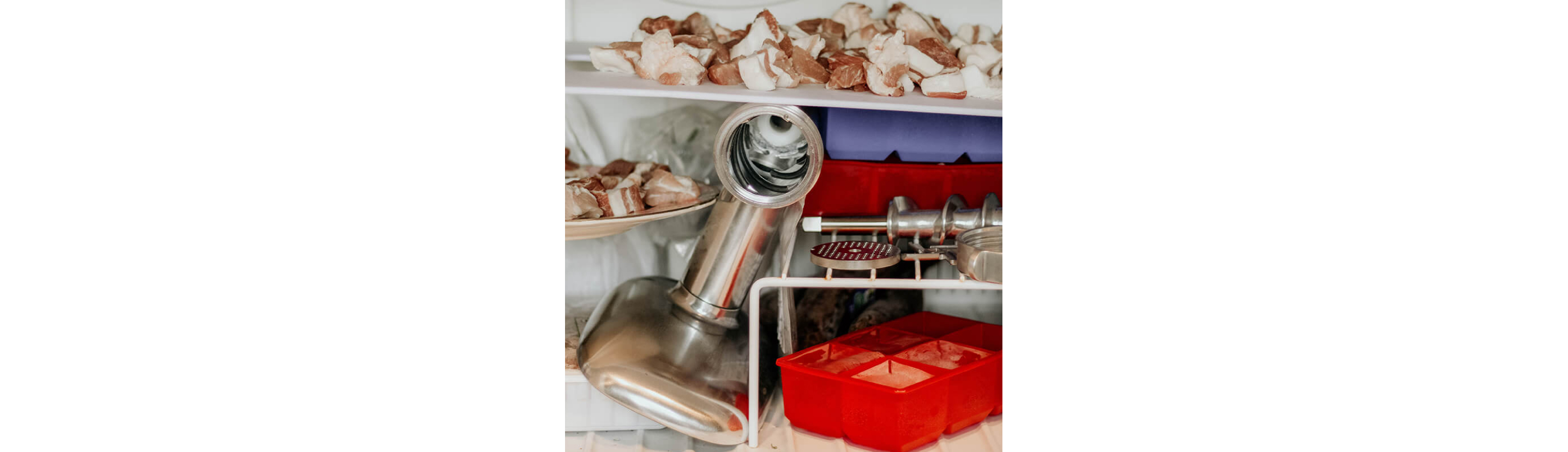 A freezer filled with uncovered meat and a KitchenAid® food grinder.