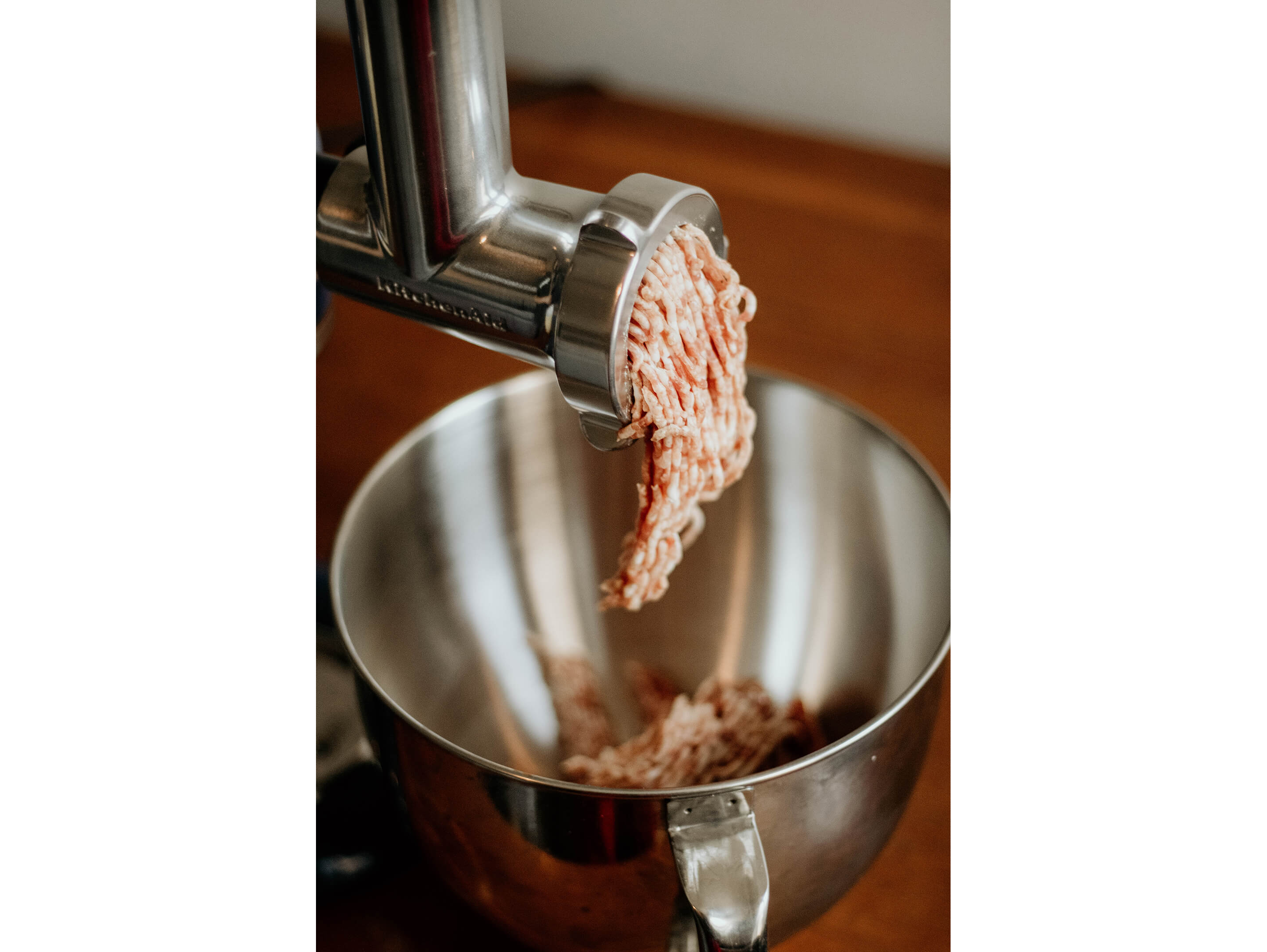 A KitchenAid® food grinder gently grinding meat into a bowl.