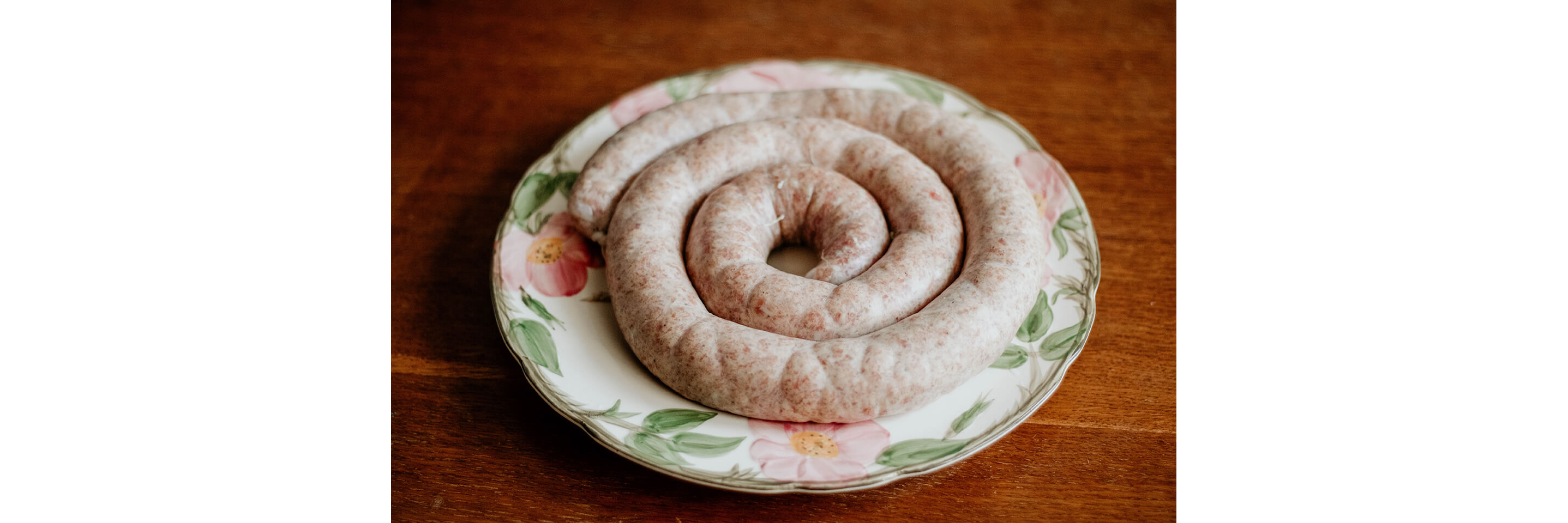 Freshly made sausage resting on a floral china plate.