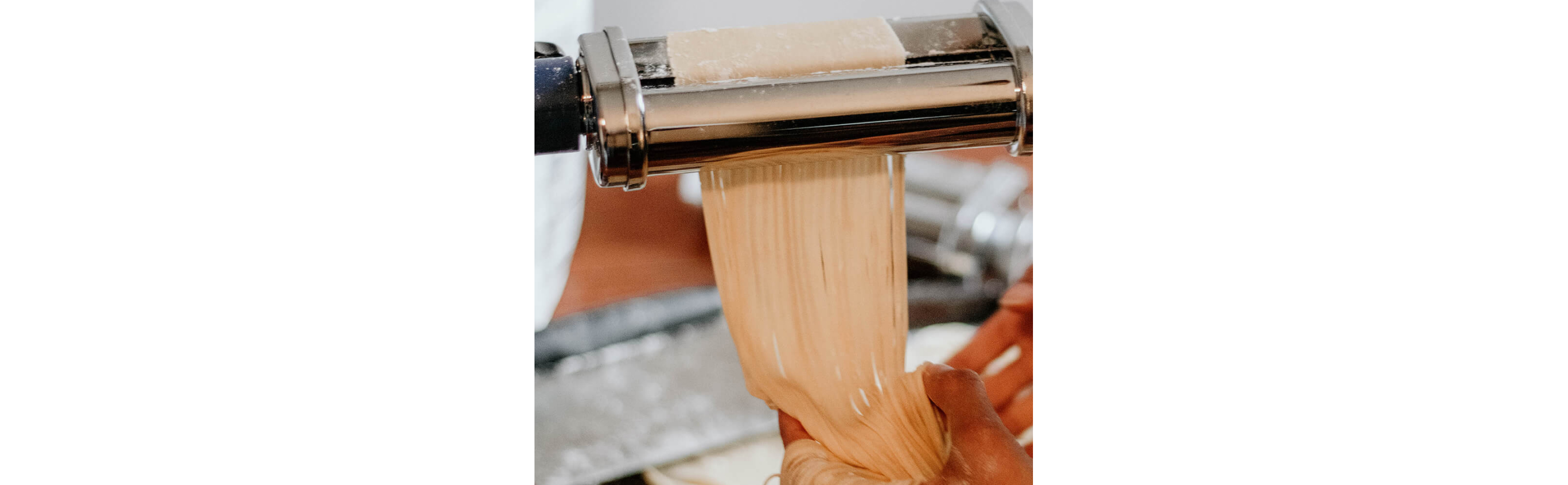 A person making homemade pasta with a KitchenAid® pasta roller attachment.