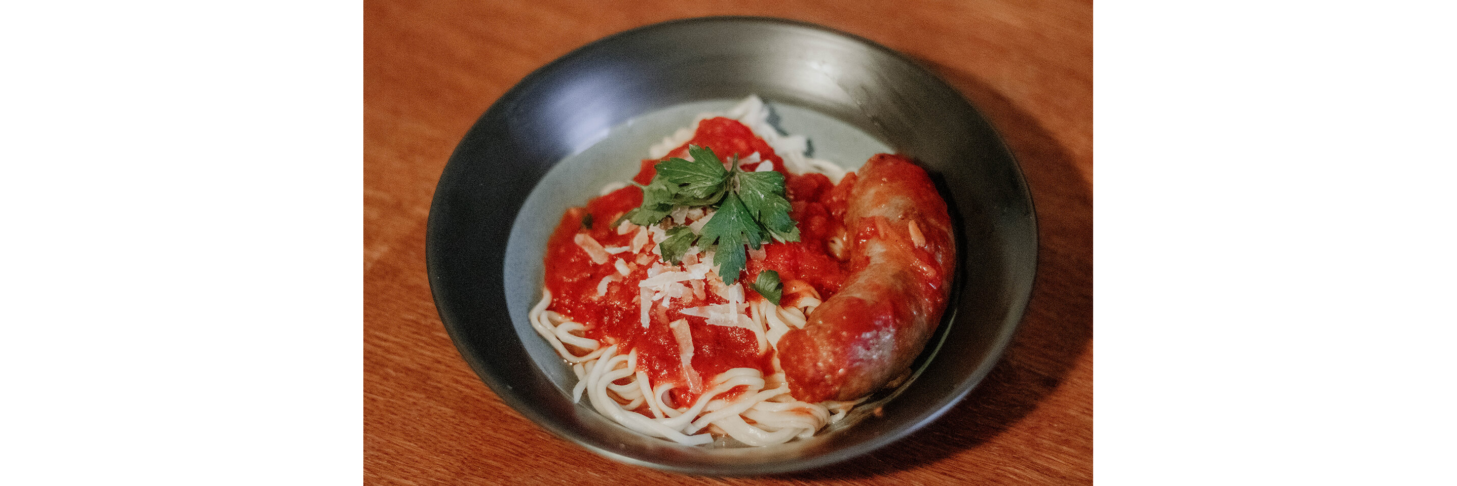 A bowl of freshly made pasta served with sauce and cooked sausage.