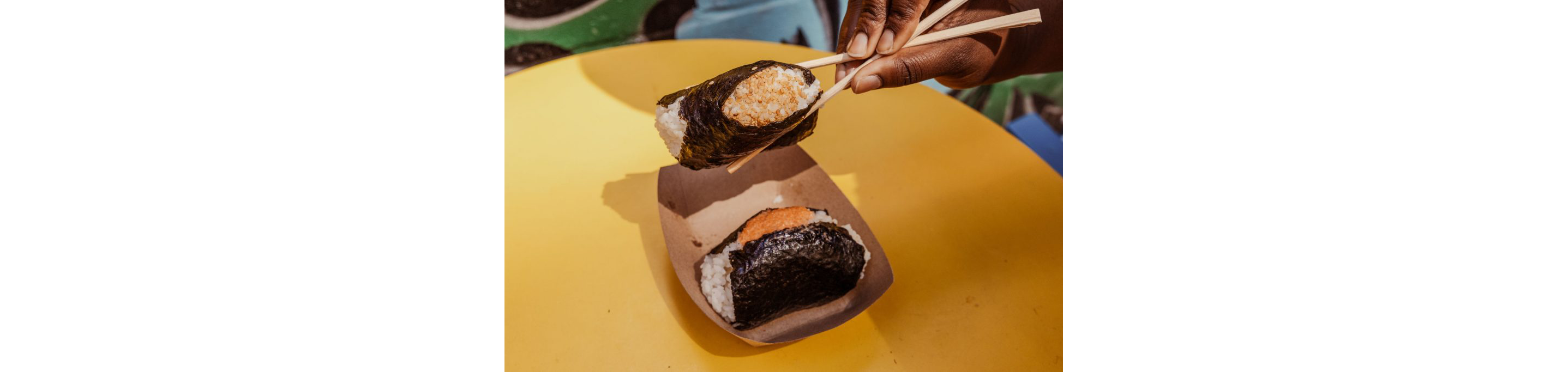 A person holding a rice ball in between two chopsticks.