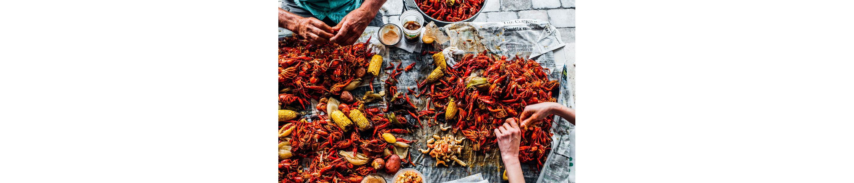 Seafood boil with shrimp, crab, crawfish and corn spread across newspaper laid out on a table.
