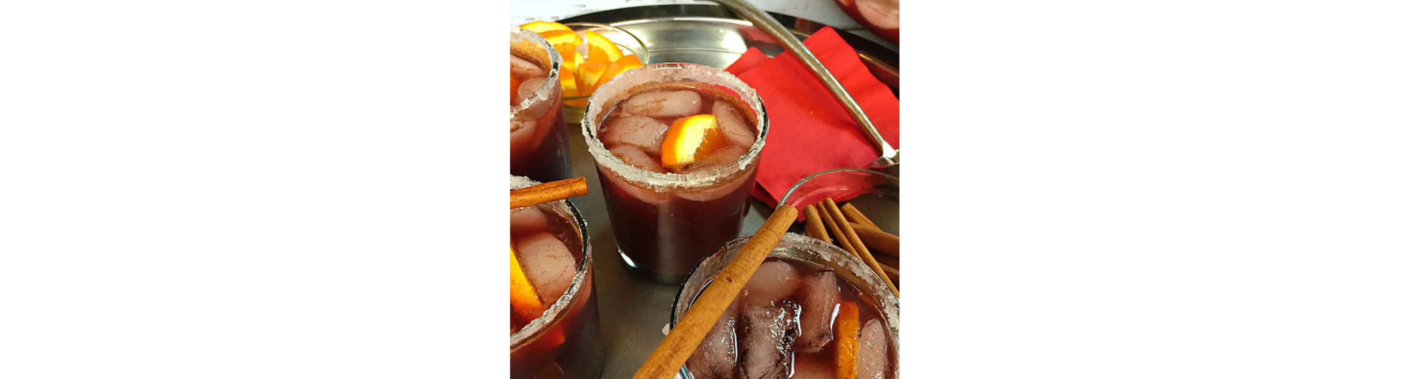 A cocktail with a salted rim, cinnamon sticks and orange slices.