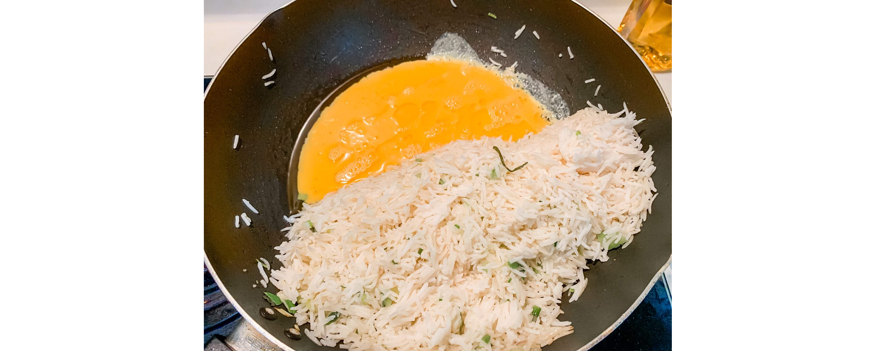 Egg, white rice and green onions frying in a wok.