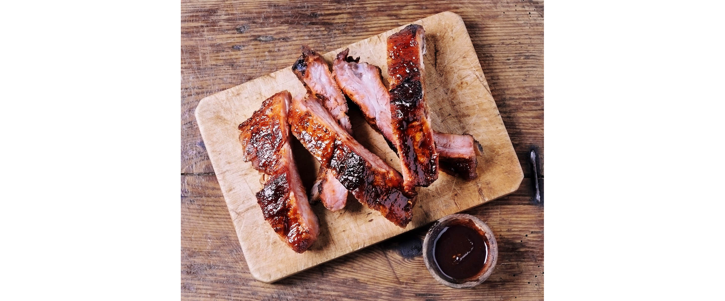 A sliced rack of barbeque ribs resting on a wooden cutting board.