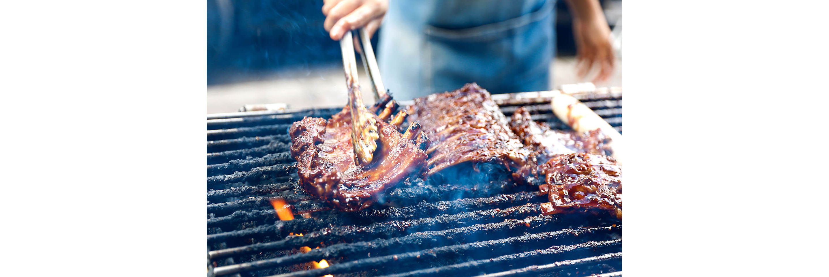 A rack of juicy ribs being turned over by tongs on a hot grill.