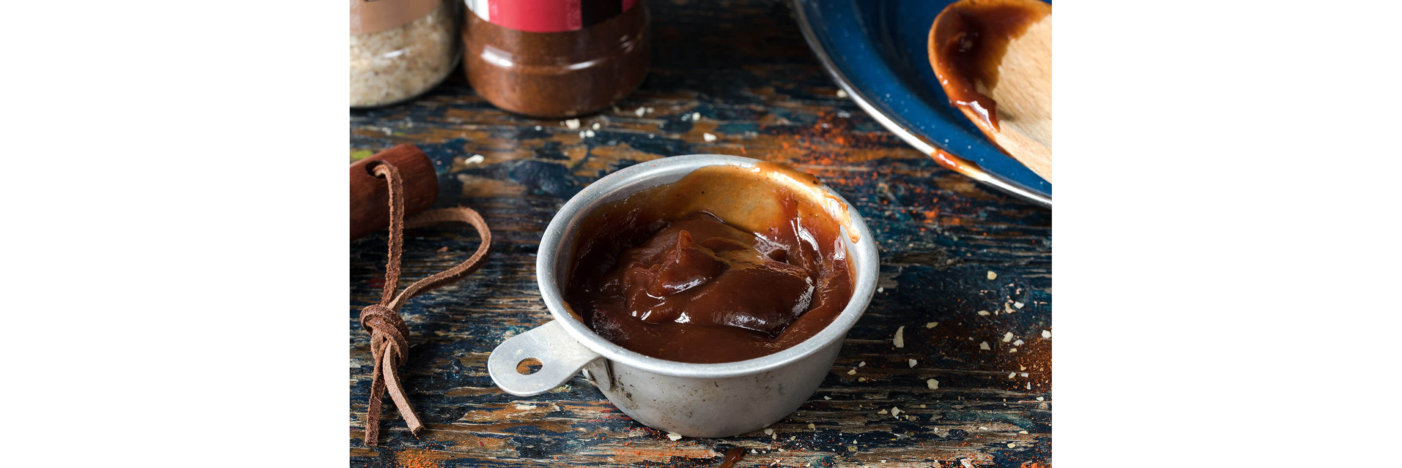 Barbeque sauce resting in a small metal bowl on a wooden table.