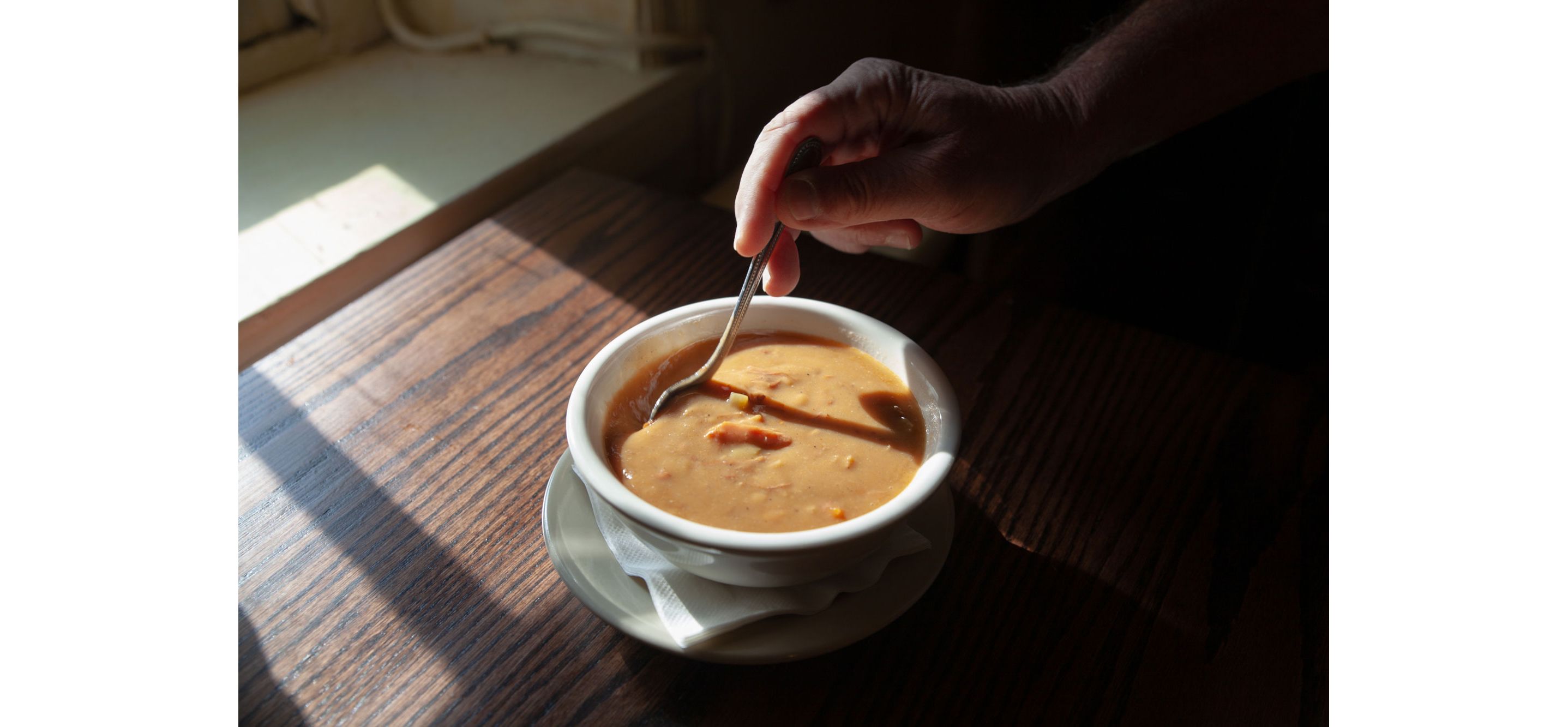 A person stirring a spoon in a small bowl of snapper soup.