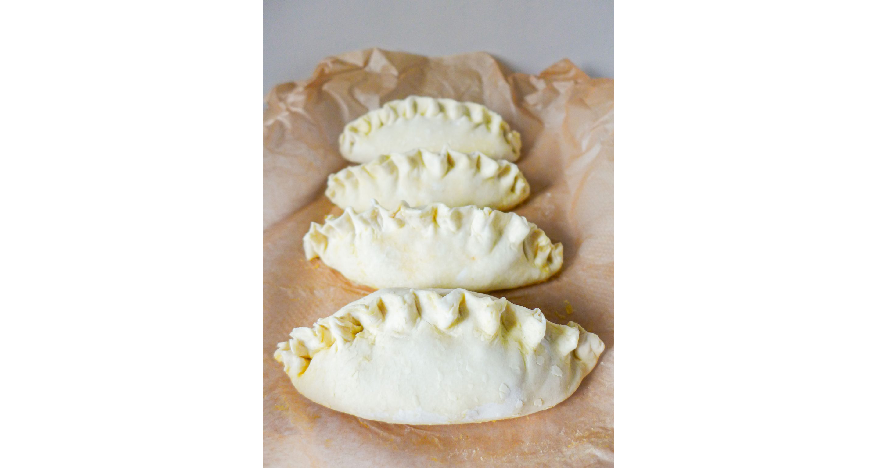Four uncooked crab pasties resting on parchment paper.