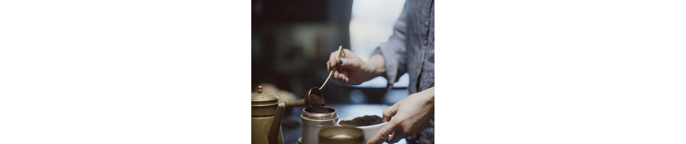 Erica pouring spoonfuls of ground coffee into a small metal carafe.