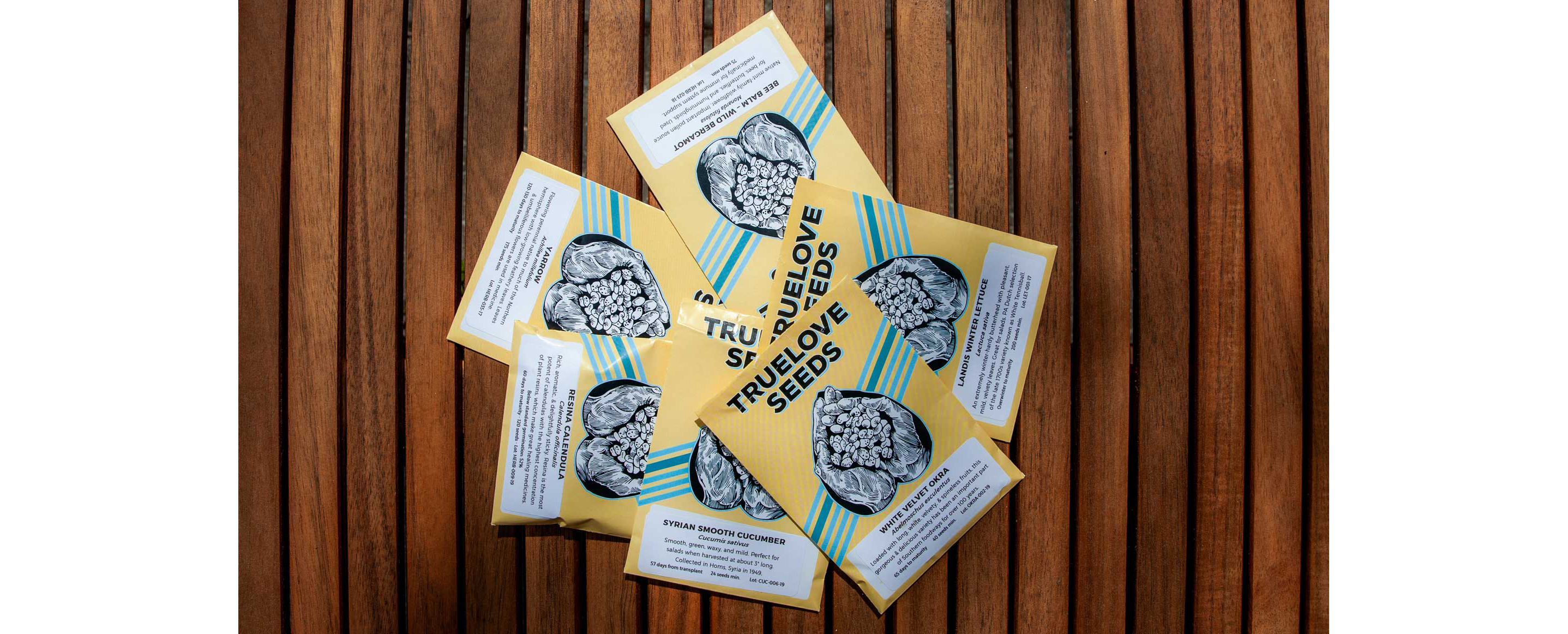 Six individual packets of True Love Seeds resting on a wooden table.
