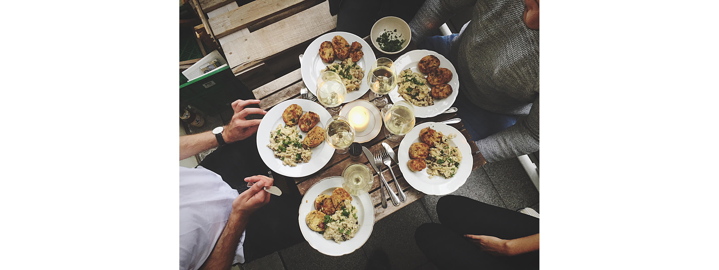 A circle of friends seated arounding a small table filled with food.
