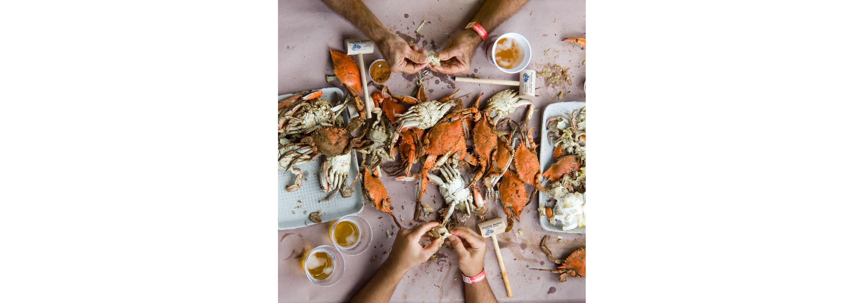 A crab boil feast strewn about a table as a person enjoys.