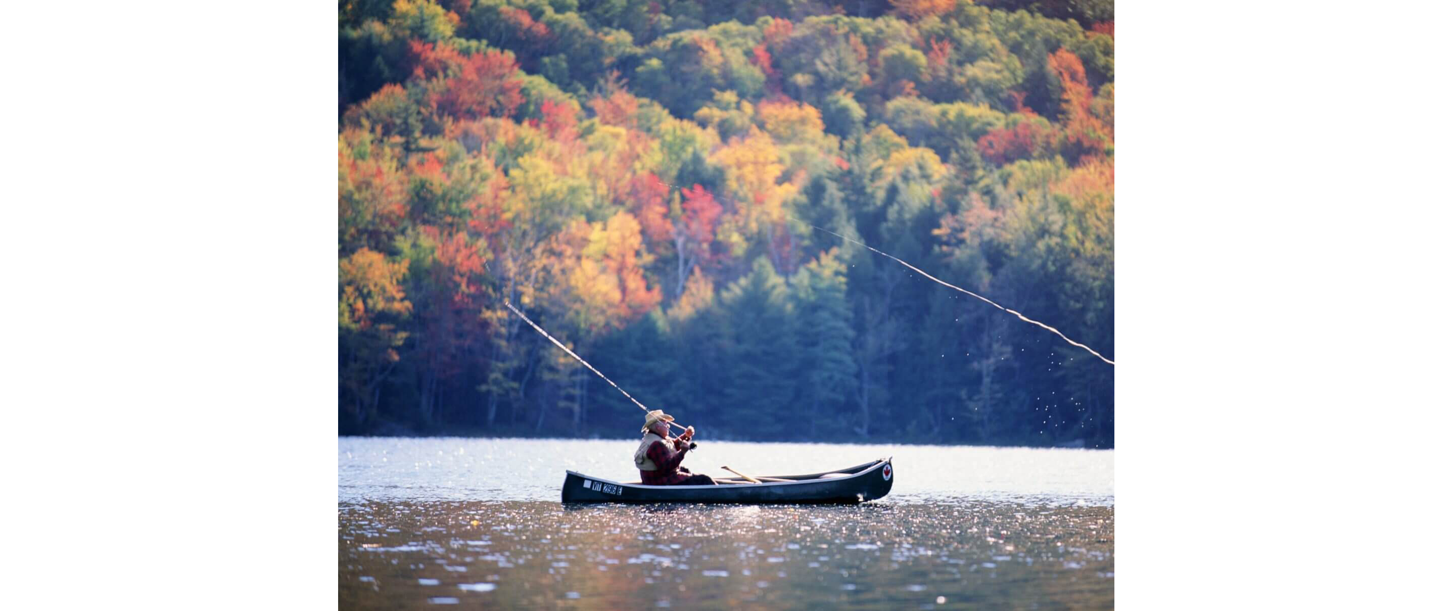 An elderly man in straw hat fishing in a canoe on a calm lake.