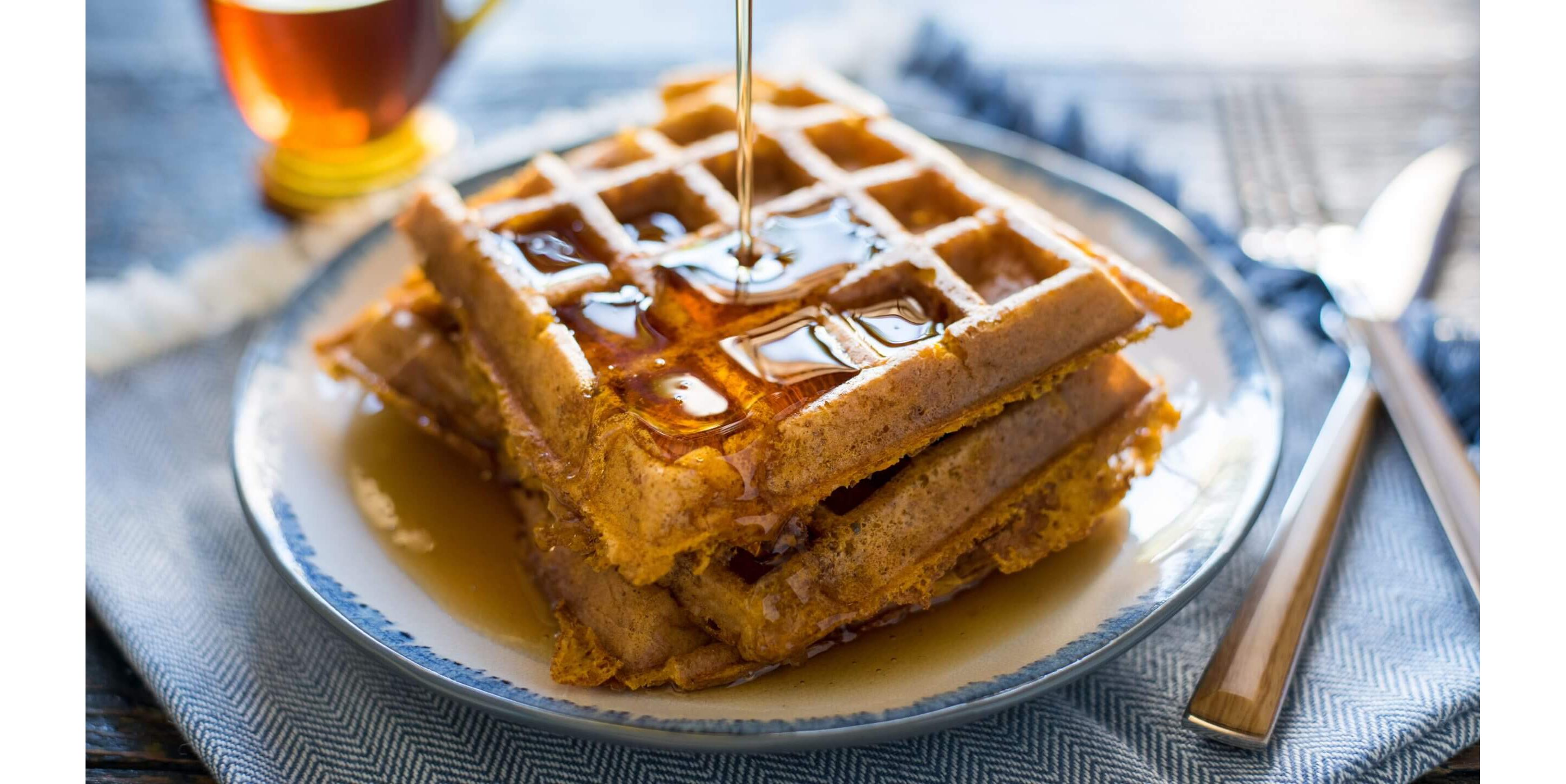 A close-up of freshly made, crispy waffles being doused in in silky syrup.
