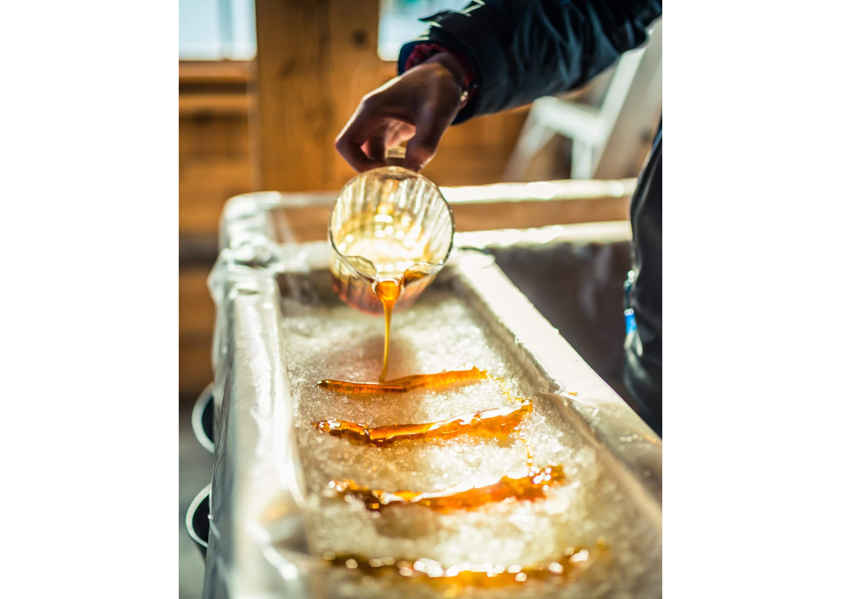 A close-up of a person gently pouring rows of syrup into packed snow for a sweet treat.