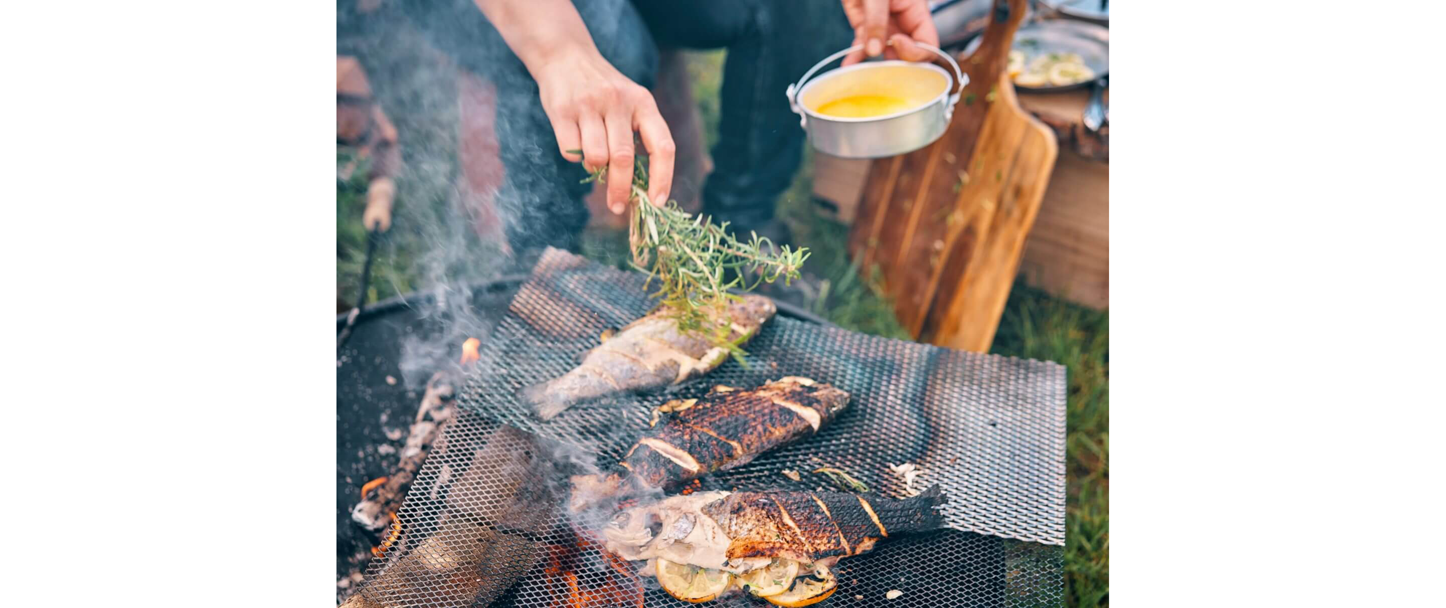 A person grilling three freshly caught fish stuffed with sliced lemons over an open fire pit.