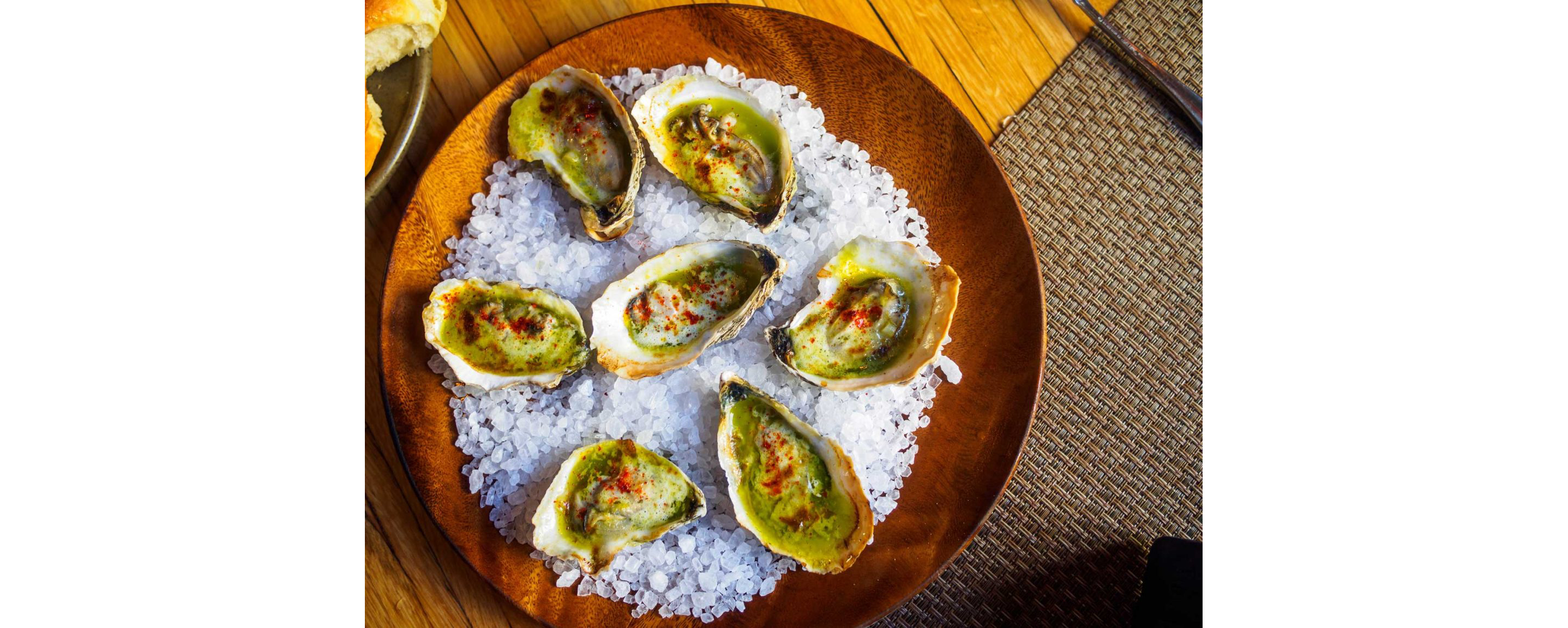 A wooden plate filled with seasoned oyster halves.