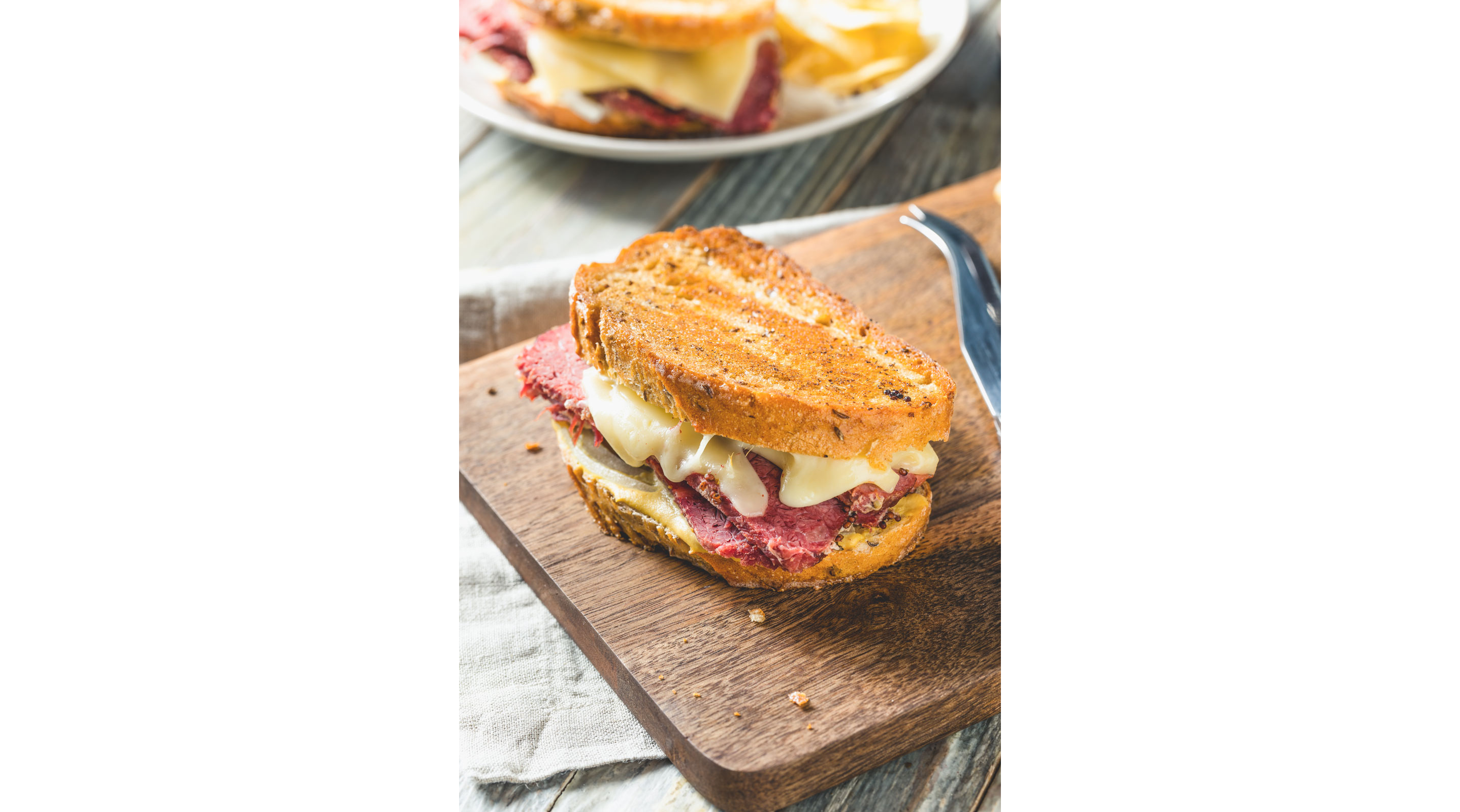 A corned beef sandwich with melted cheese on a wooden cutting board.