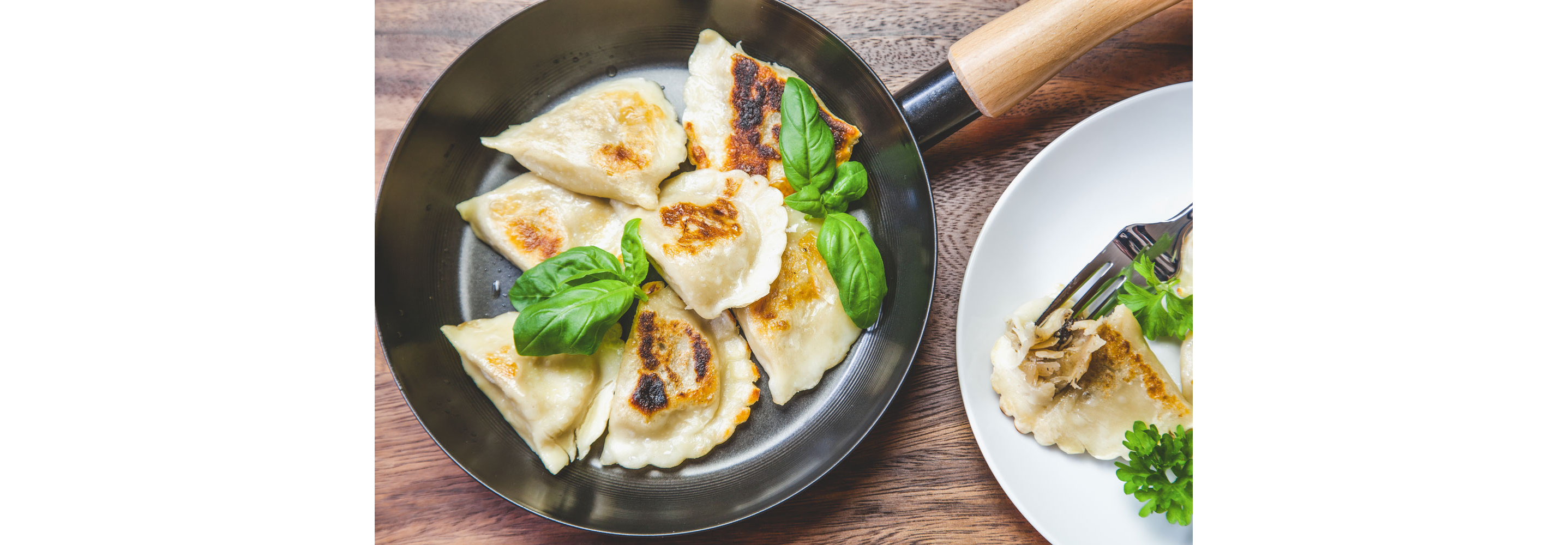 A pan filled with fried pierogies garnished with basil.