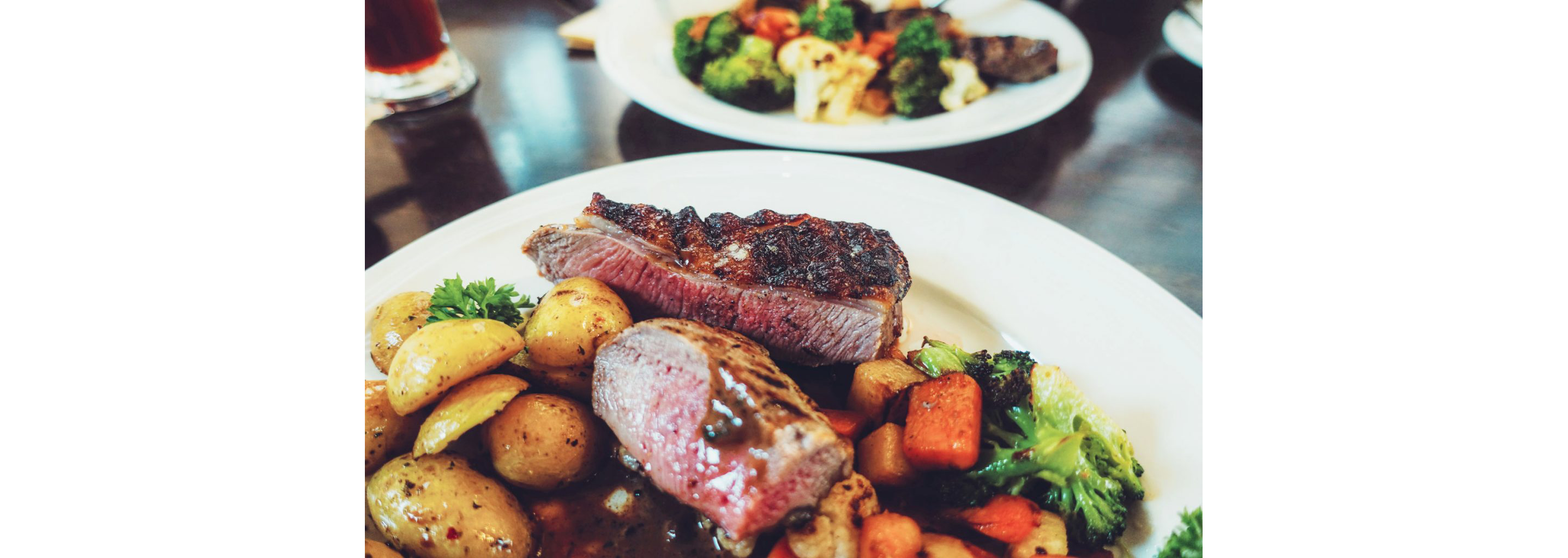 A white plate filled with grilled meat, potatoes and other vegetables.