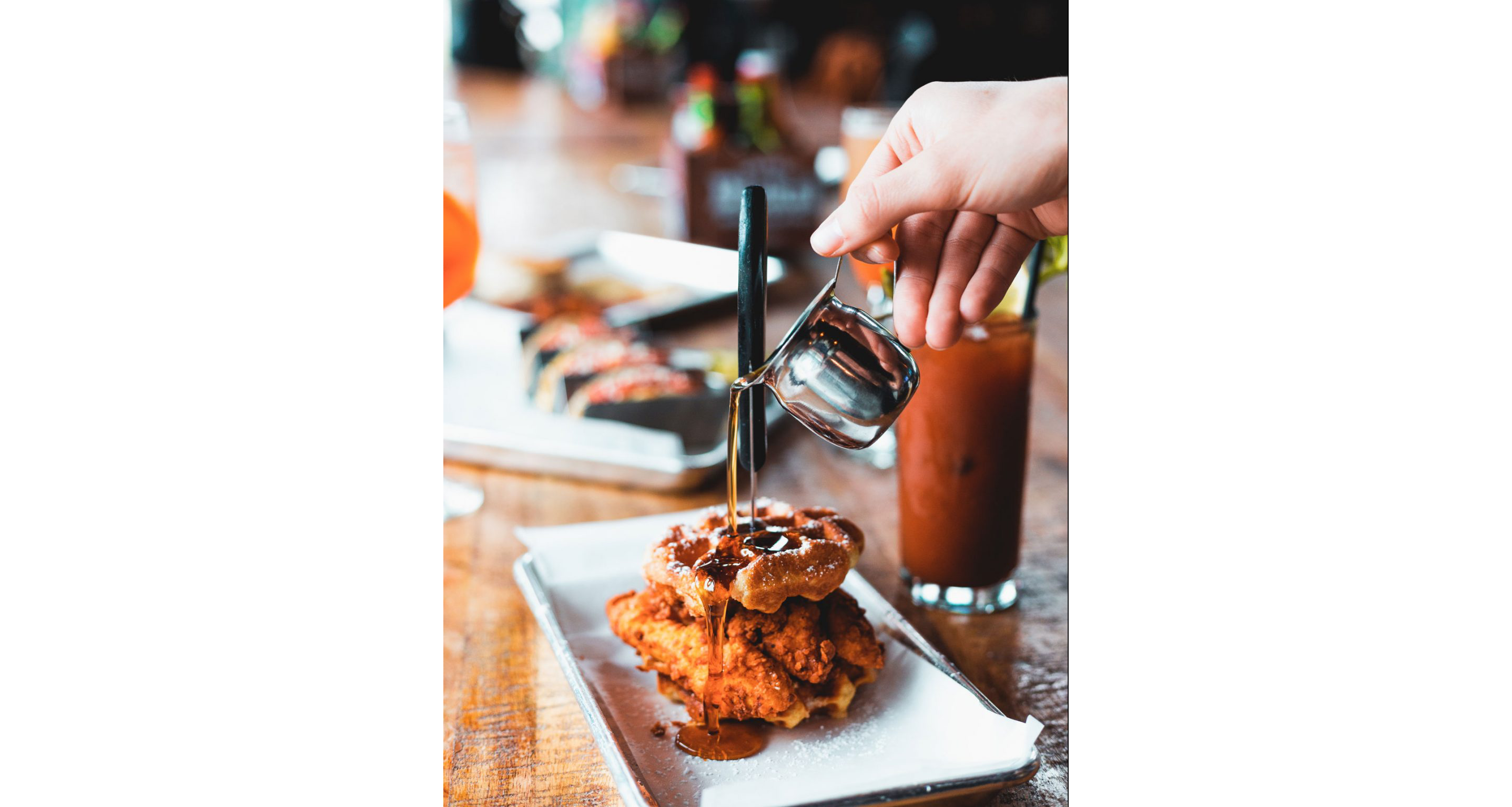 A person pouring syrup on a plate of chicken and waffles.