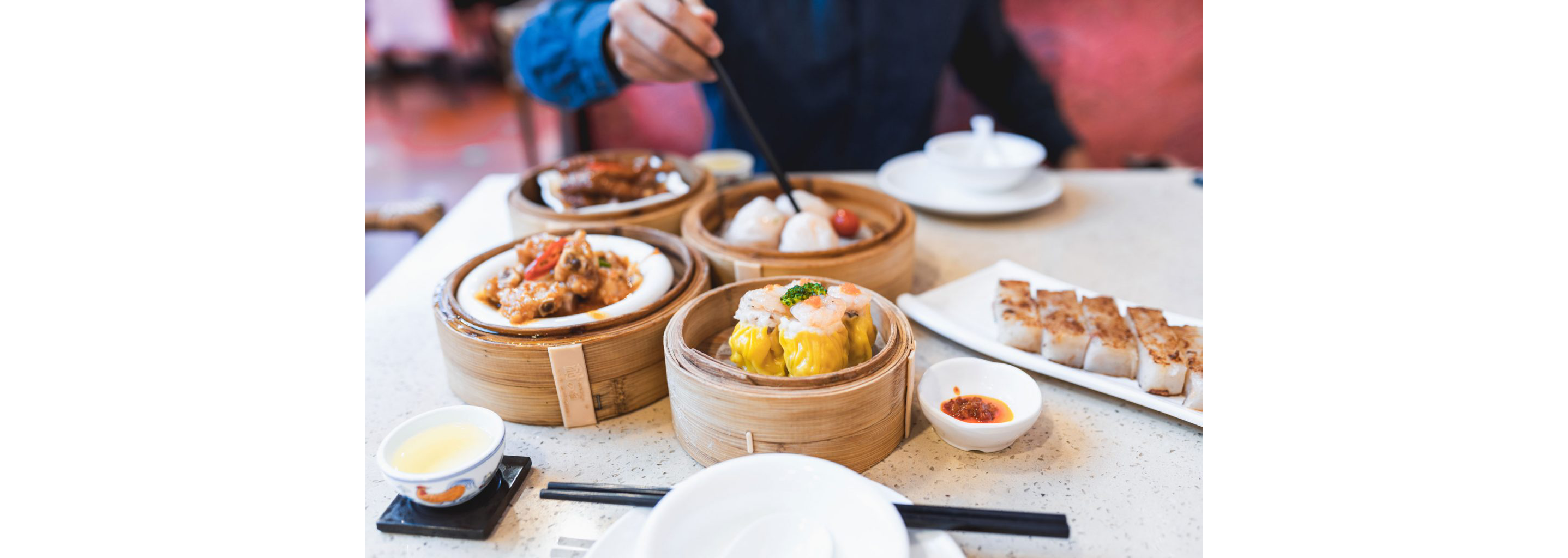 A person enjoying lavish dishes of dim sum with another person.
