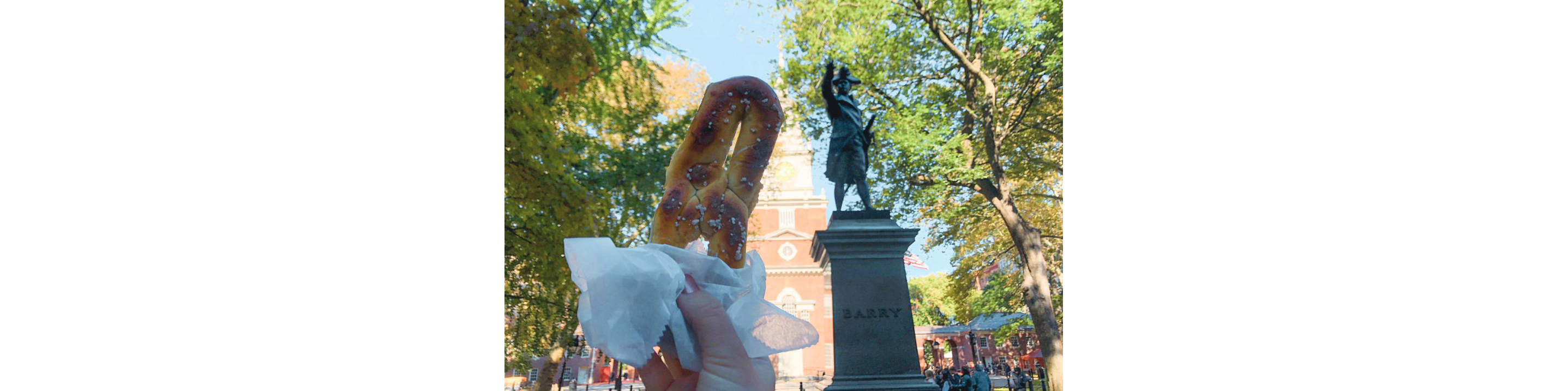 A person holding up a wrapped pretzel.