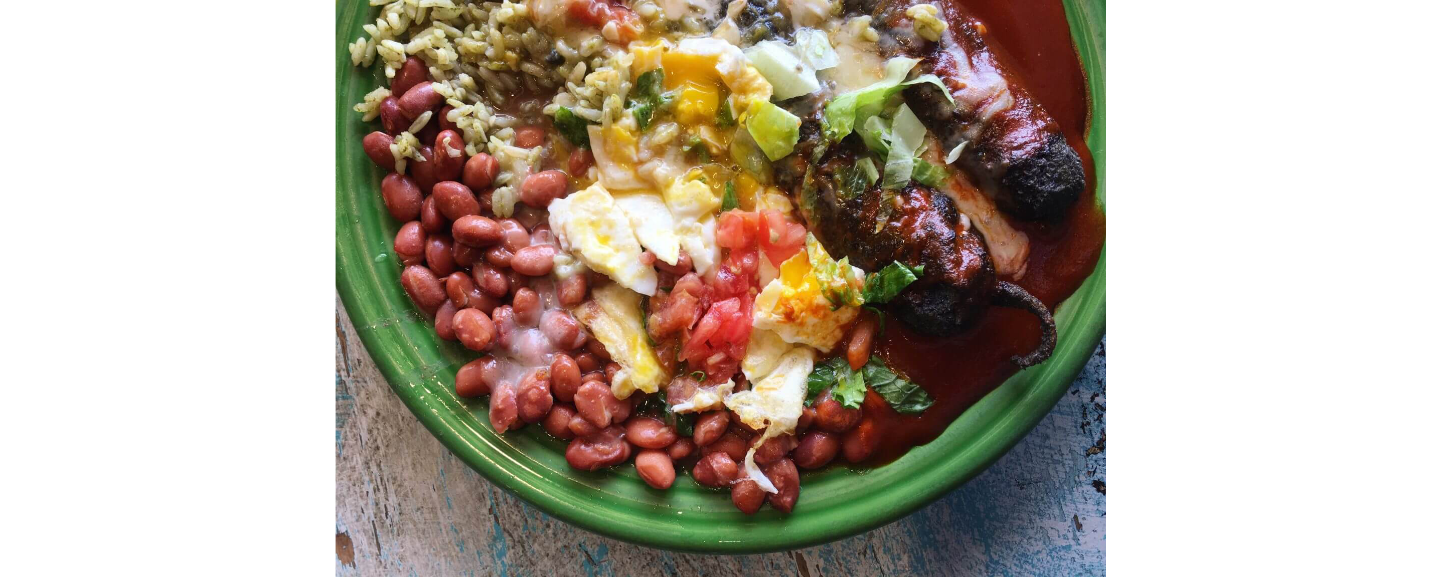 A green plate filled with beans, rice and grilled peppers topped with eggs and pico de gallo.