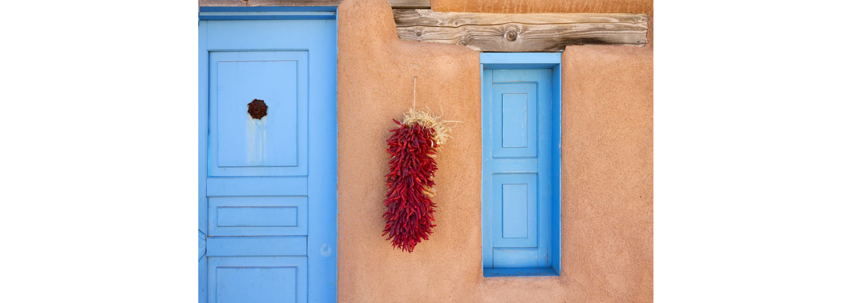 An adobe constructed household adorned with a batch of hanging dried, red chile peppers.