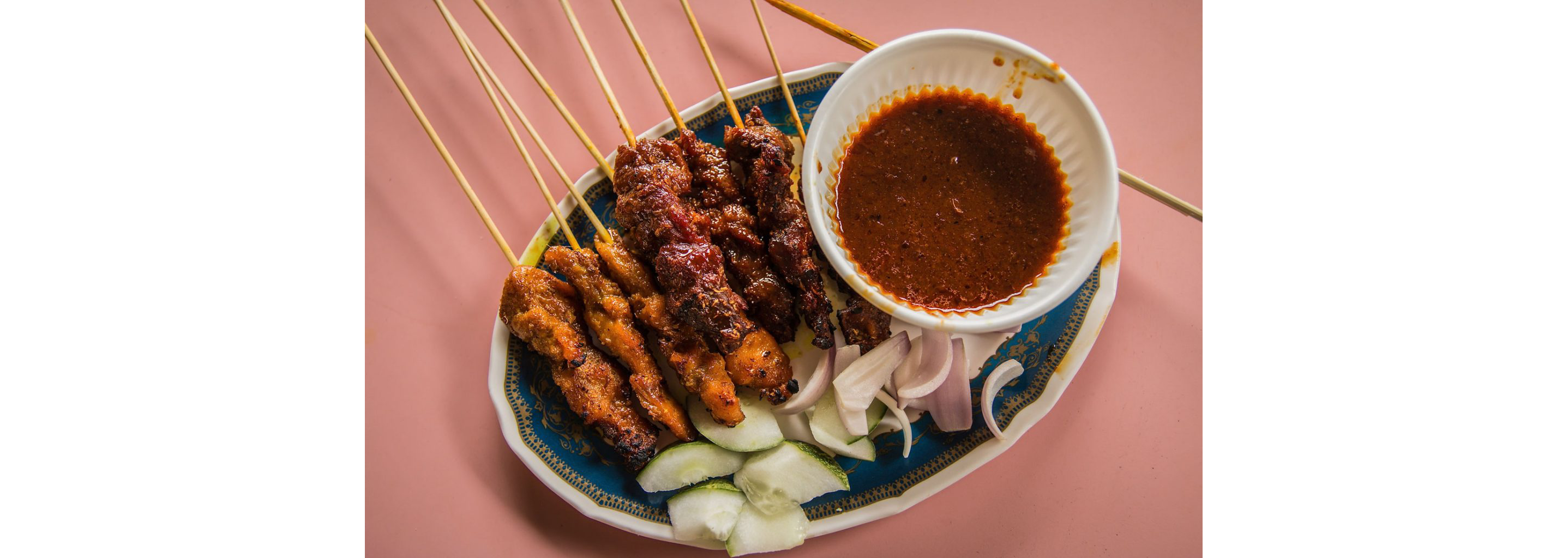 An ornate dish filled with Singaporean satay and a dish of peanut sauce.