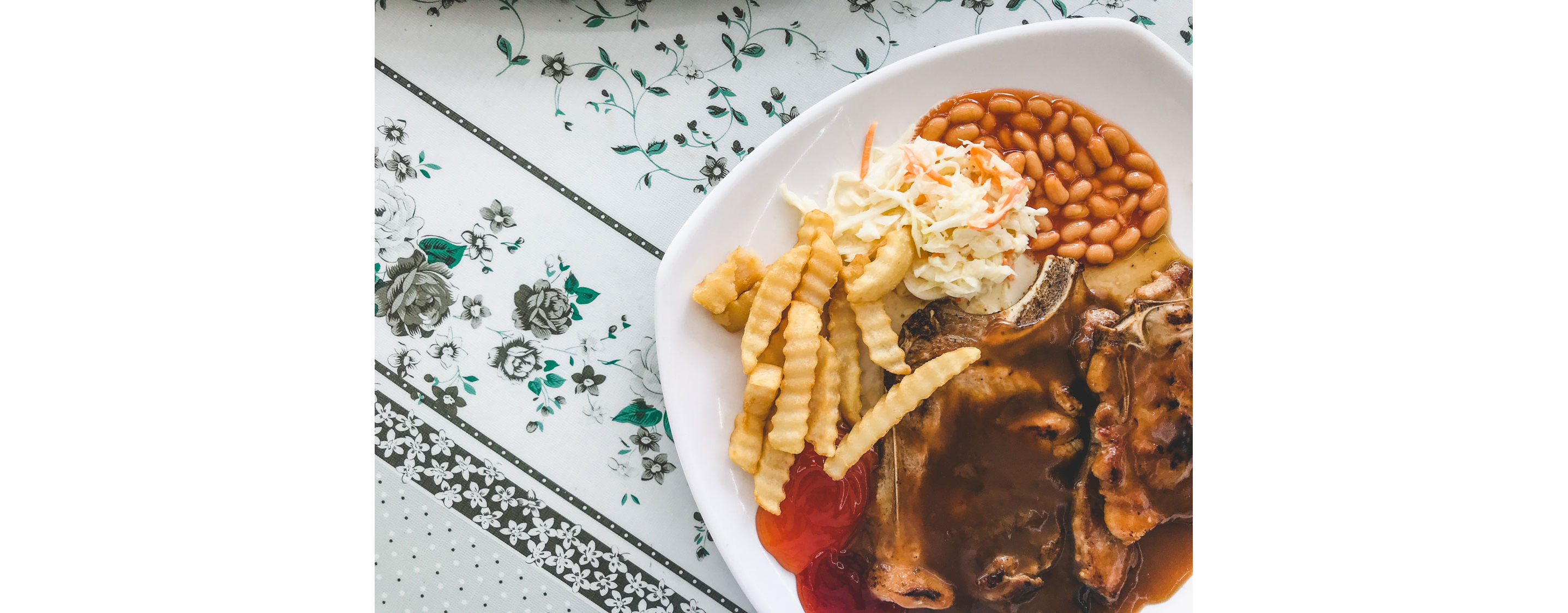 A plated porkchop in brown sauce served with crinkle-cut fries, baked beans and coleslaw.