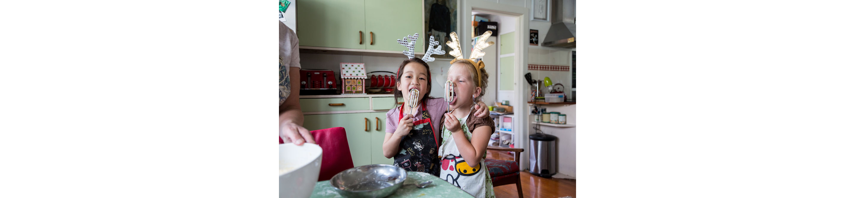 Two young children licking batter off of mixing beaters.
