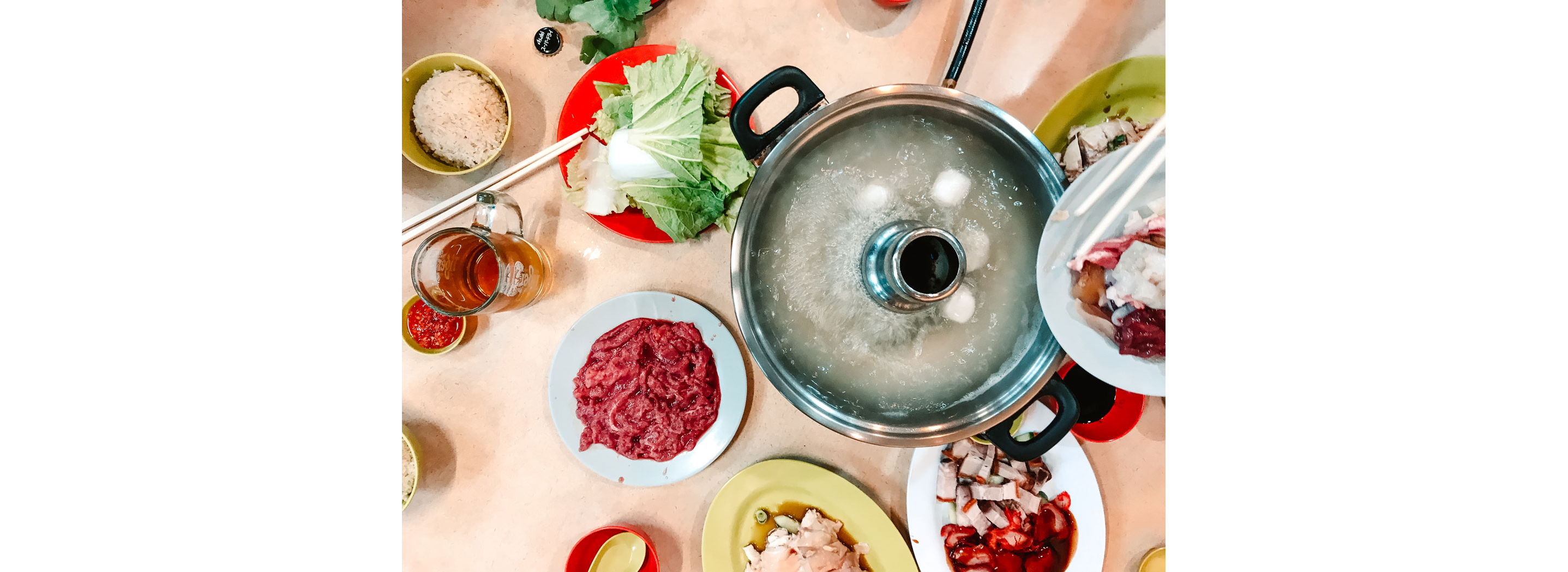 A boiling steamboat surrounded by raw vegetables and meats.
