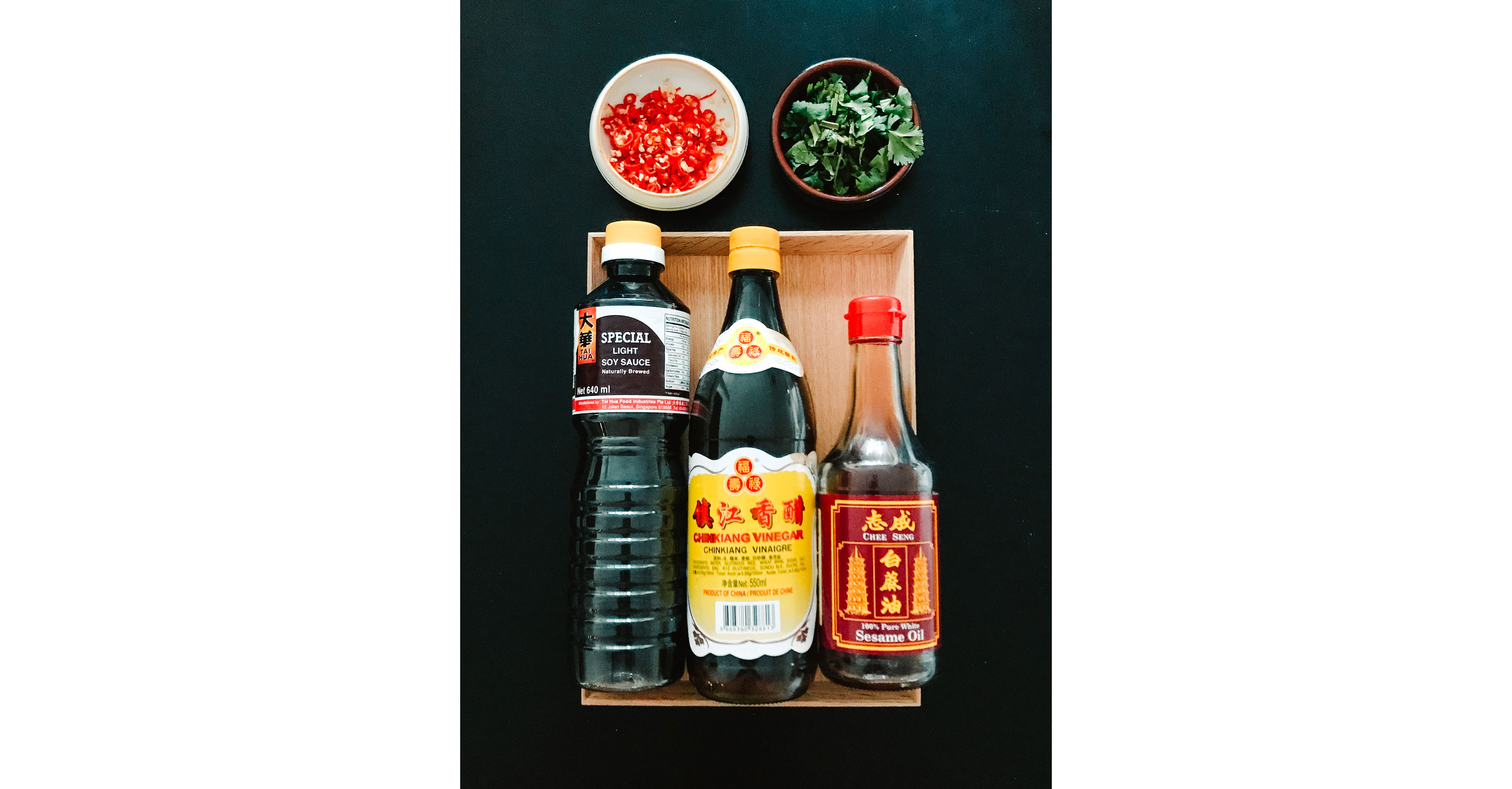 A bottle of sesame oil, soy sauce and black vinegar with small dishes of chili rings and coriander.