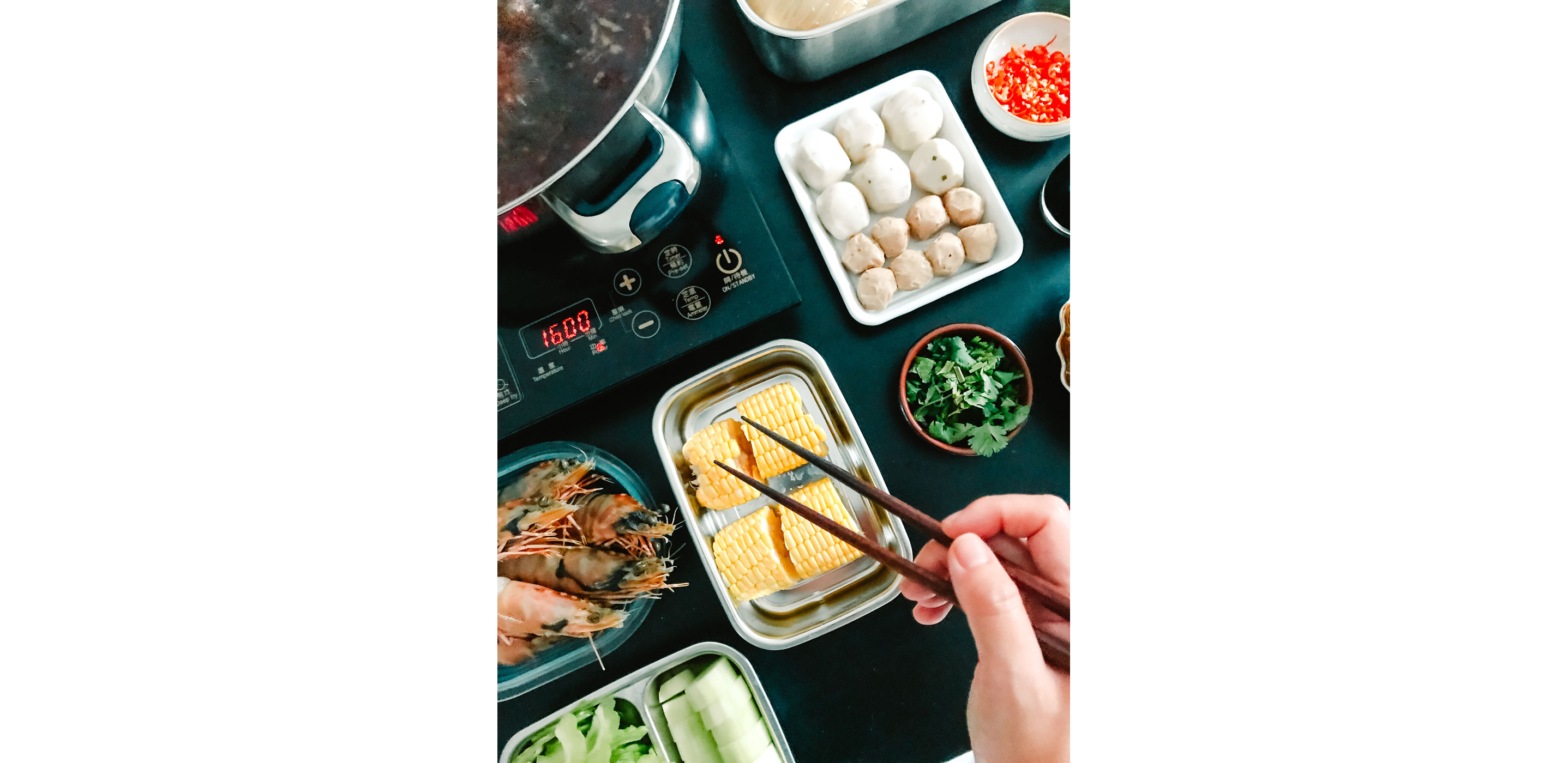 A black table with trays of raw corn, prawns and other ingredients.