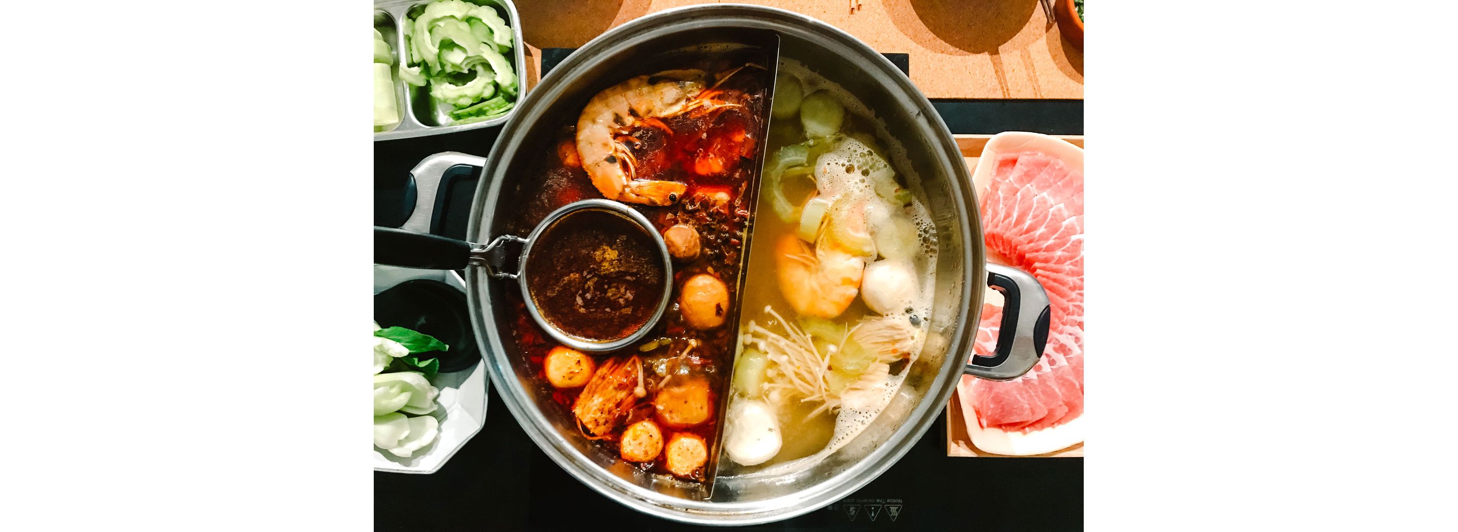 A steamboat, or hotpot, resting on a table with various raw ingredients.