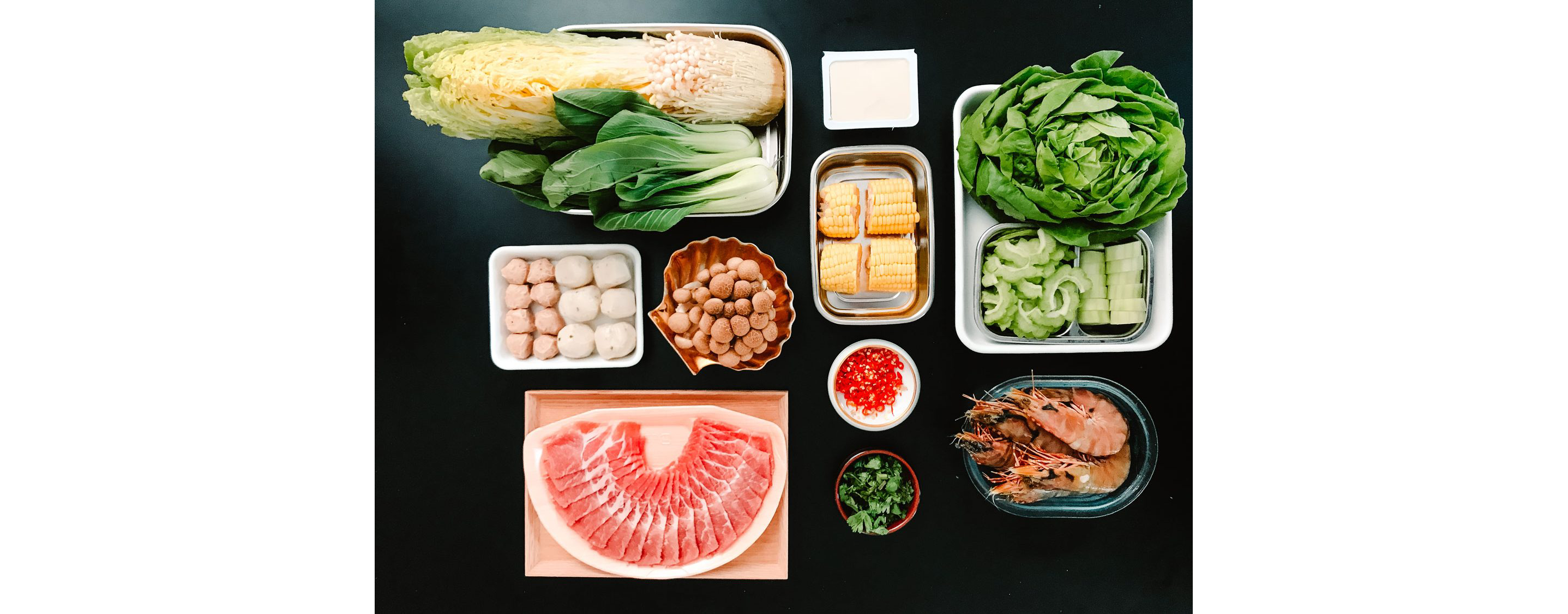 A black table with small trays of raw vegetables, meats and other ingredients.