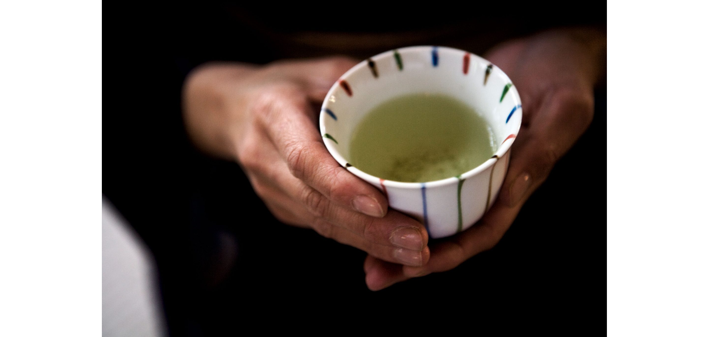 Calm hands holding a small ceramic cup filled with green tea.