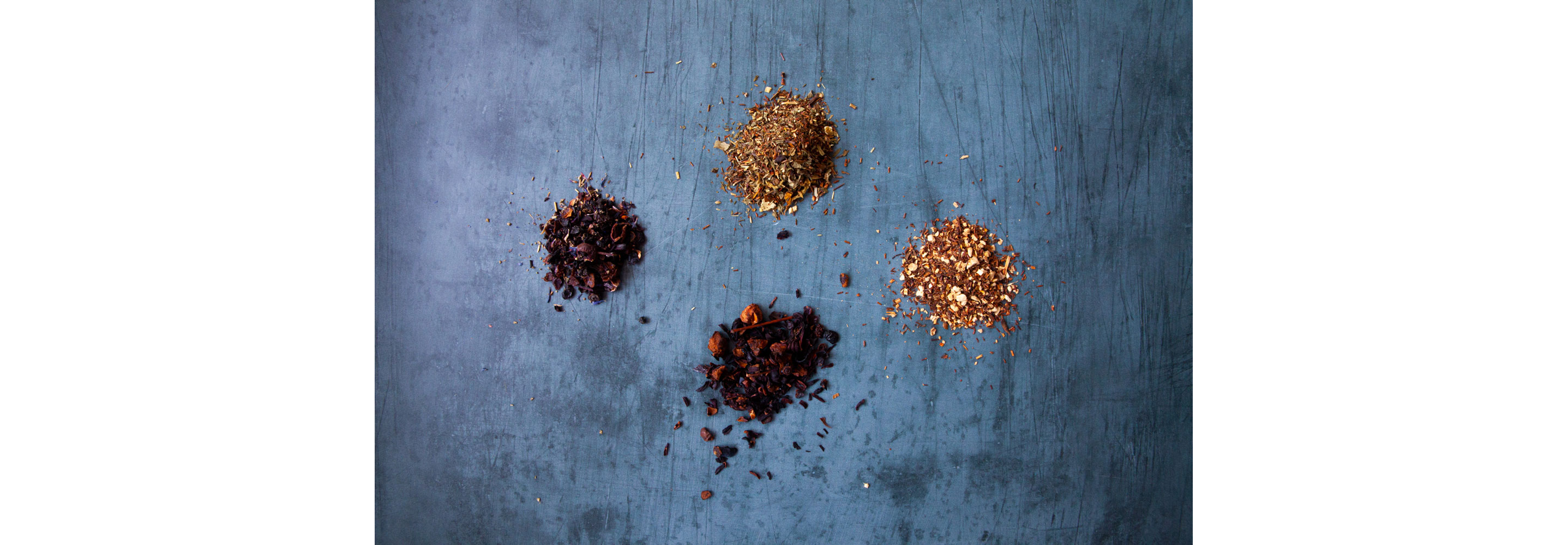 Four separate piles of various dried tea leaves.
