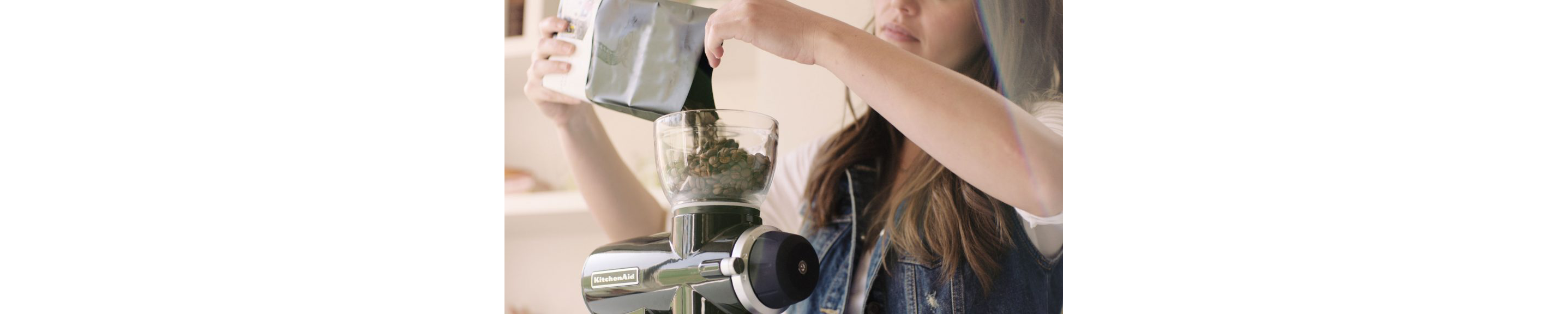 A young woman pouring a small bag of coffee beans into a KitchenAid® Burr Grinder.
