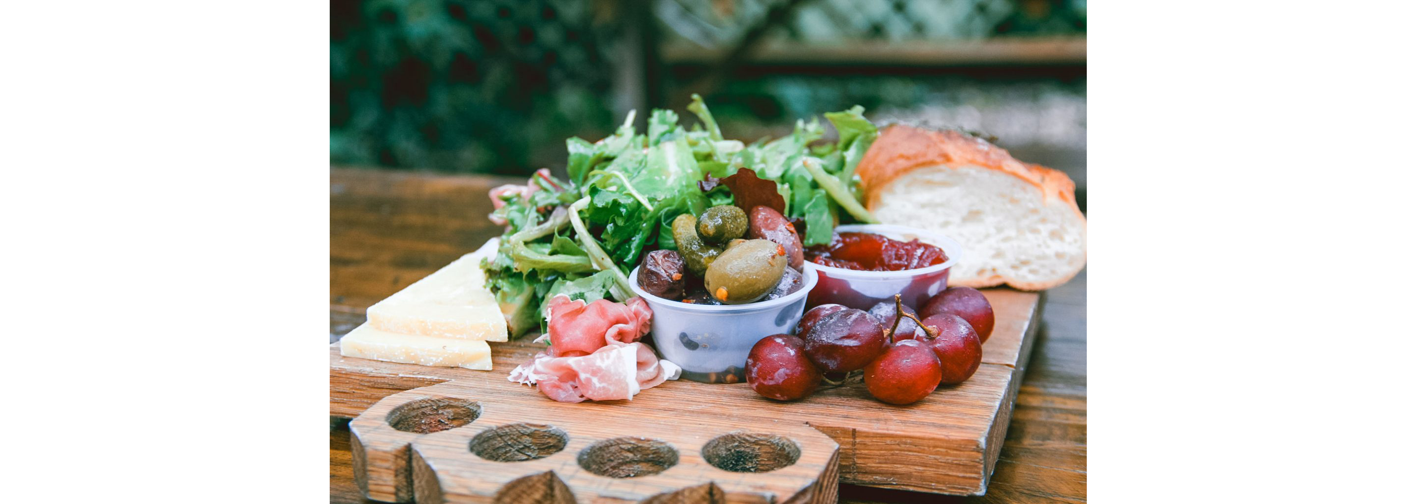Meat and cheese board with bread, lettuce and grapes.