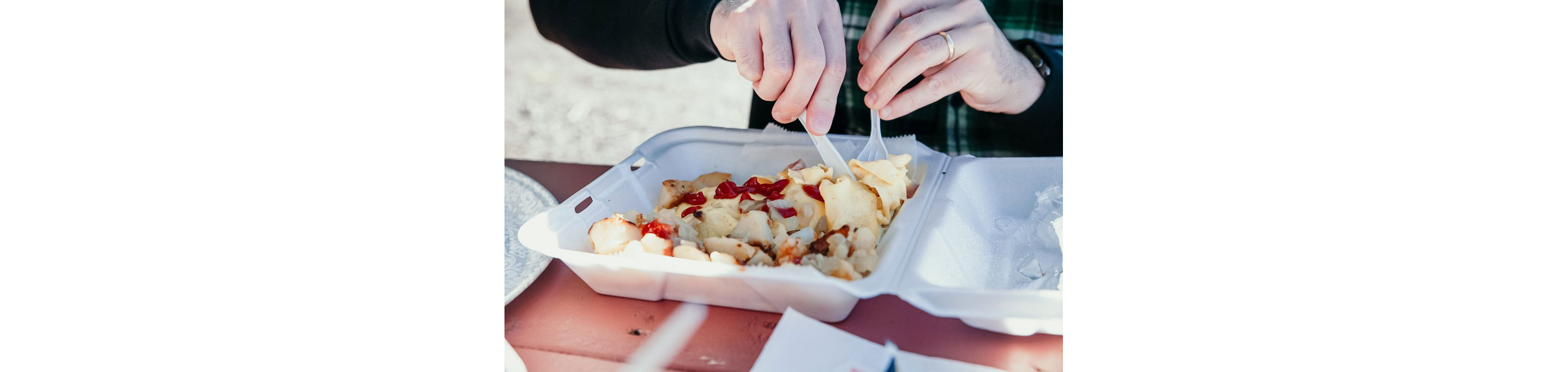 A person digging into their takeaway container of food with a knife and fork.